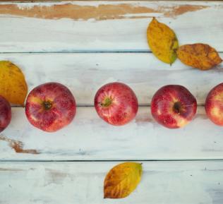 Five apples on a white table with fall leaves surrounding them.
